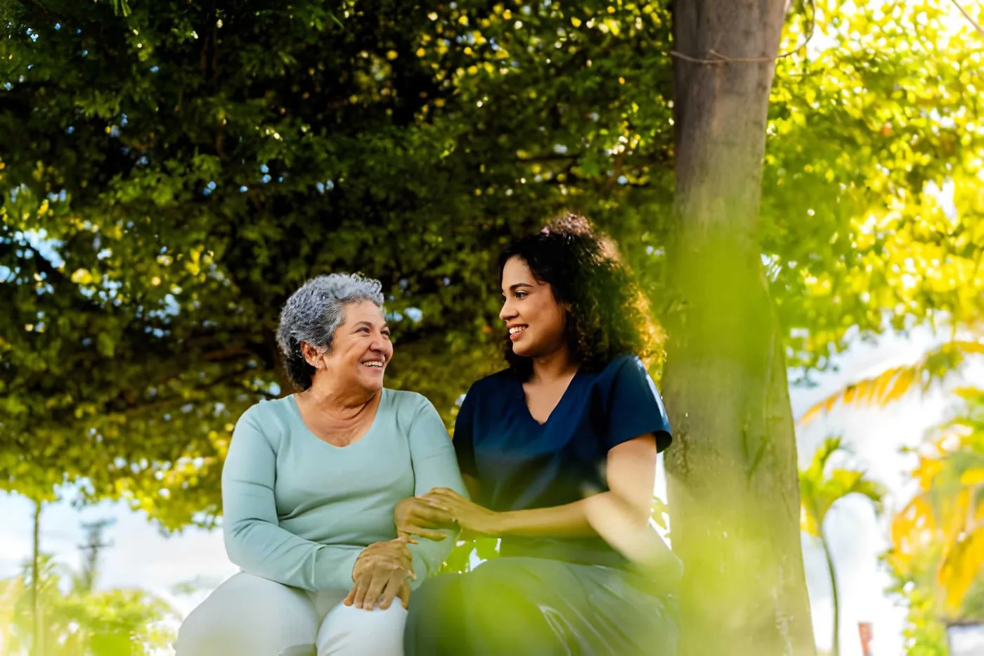 An older adult and care professional talking together in a leafy park