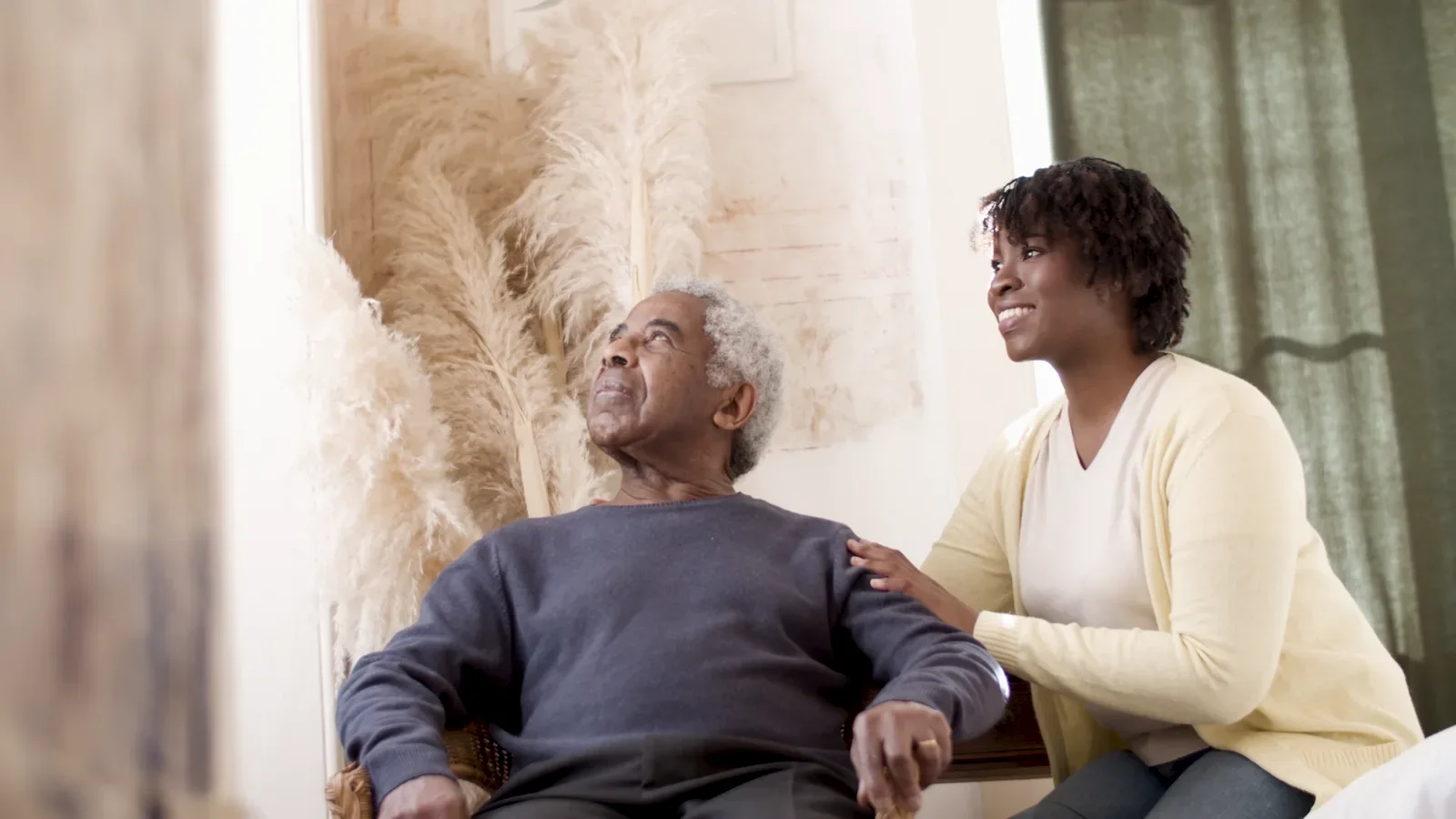 A care professional sitting beside and talking with an older adult at home